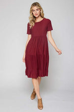 full body view of short sleeve burgundy with dot textured short dress that goes to knees. cinches at the small of the waist and flows out tiered on the bottom half