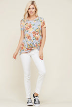 full body view of greyish lavender shortsleeve top with floral print and a twist hem at the bottom