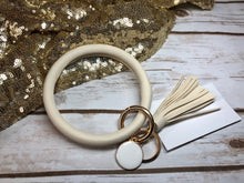 cream bangle ring keychair with tassle and monogram tag. large ring for any size wrist and easy clip for attaching keys. contains two 2 rings to attach keys to. monochromatic, cute, and fun.
