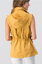 back view of mustard sleeveless collared cargo vest with 4 front pockets, draw string at waist, and hood