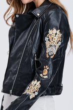 zoomed in side view of sleeve on faux leather jacket with embroidered sleeves. meets at your waist. zip up in front and tie around waist