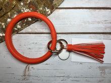 orange bangle ring keychair with tassle and monogram tag. large ring for any size wrist and easy clip for attaching keys. contains two 2 rings to attach keys to. monochromatic, cute, and fun.