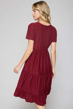 back view of short sleeve burgundy with dot textured short dress that goes to knees. cinches at the small of the waist and flows out tiered on the bottom half