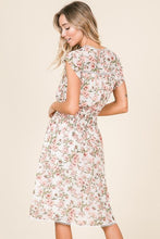 back view of ivory and floral short lined peasant dress with round neckline, fluttery cap sleeves, and a smocked waist. the back is a key hole with a button closure.  