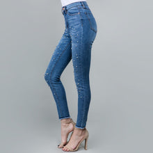 side view of blue high rise skinny jeans with stretch. fully embellished in silver and white pearls down to fray hem detail